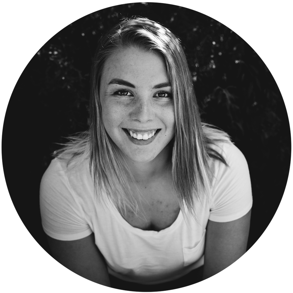 Black and white image of Arianna Augustine. The photo is a head shot showing that Arianna in a white shirt sitting in front of some sort of bush.